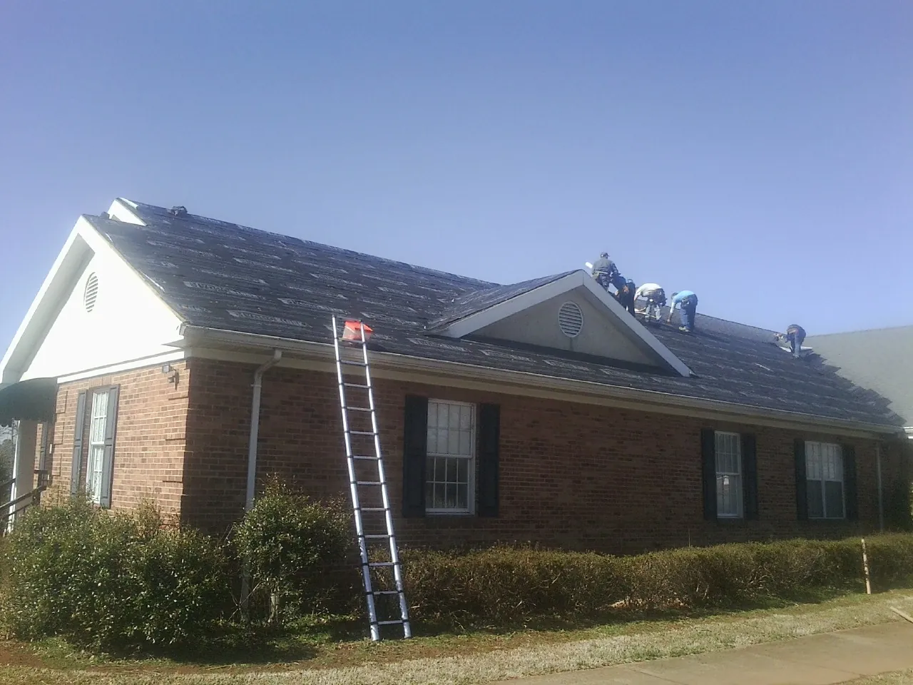 Crew tearing shingles off a brick ranch roof with a ladder set — Emergency Roof Repair work by our crew in Waite Park