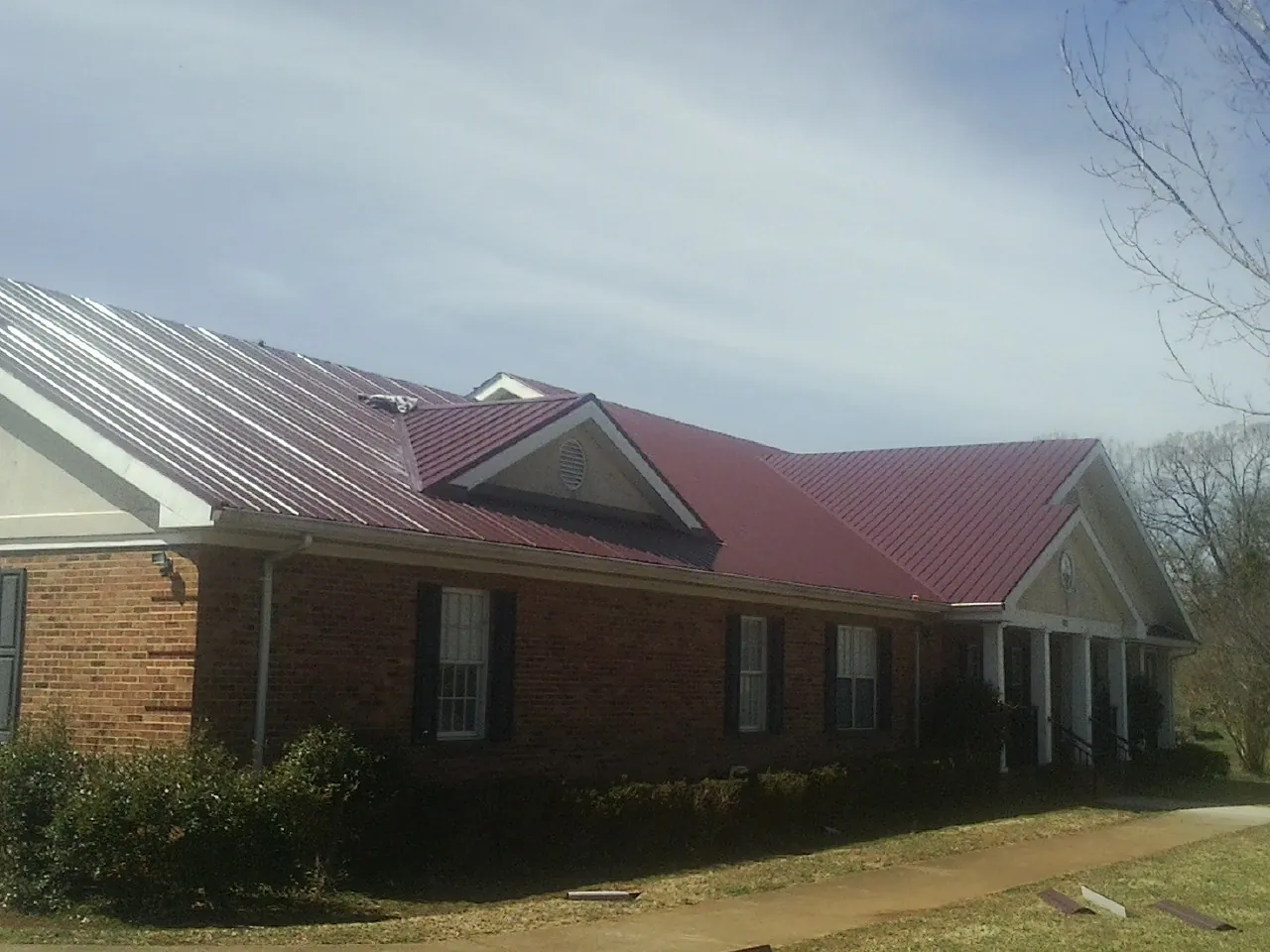 Red metal roof with gabled entries on a long brick building, from a Hail Damage Roof Repair job in Waite Park