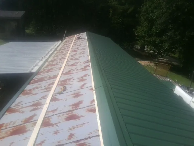 Old rusted panels beside newly installed green metal roofing — Wind Damage Roof Repair by Roofing Brothers in Waite Park