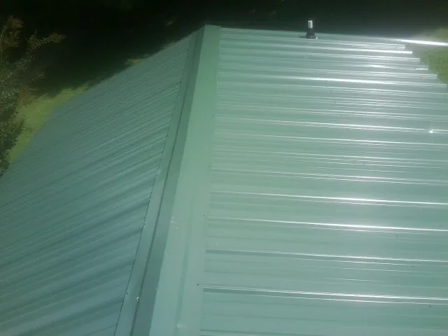 New green metal panels meeting at the ridge of a roof — Flat Roof Repair work by our crew in Waite Park