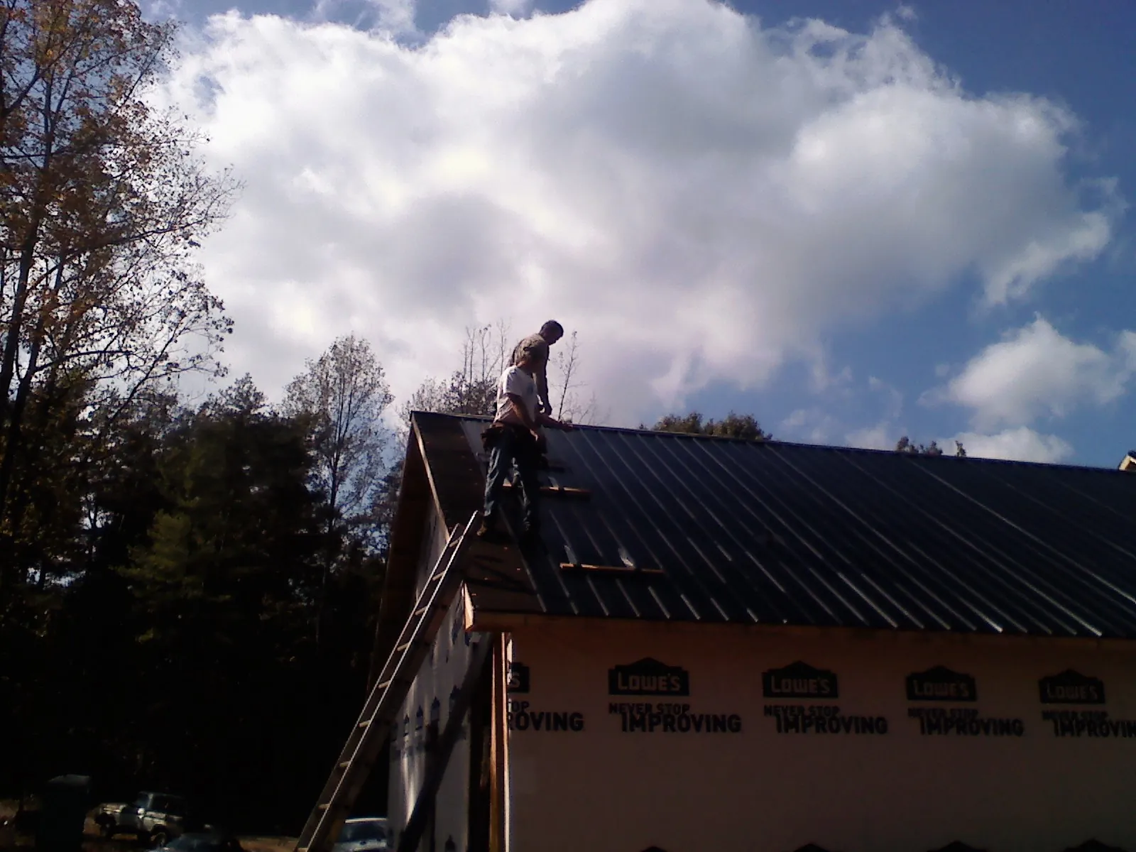Roofer fastening dark metal panels high against a cloudy sky, from a Roof Inspection job in Waite Park