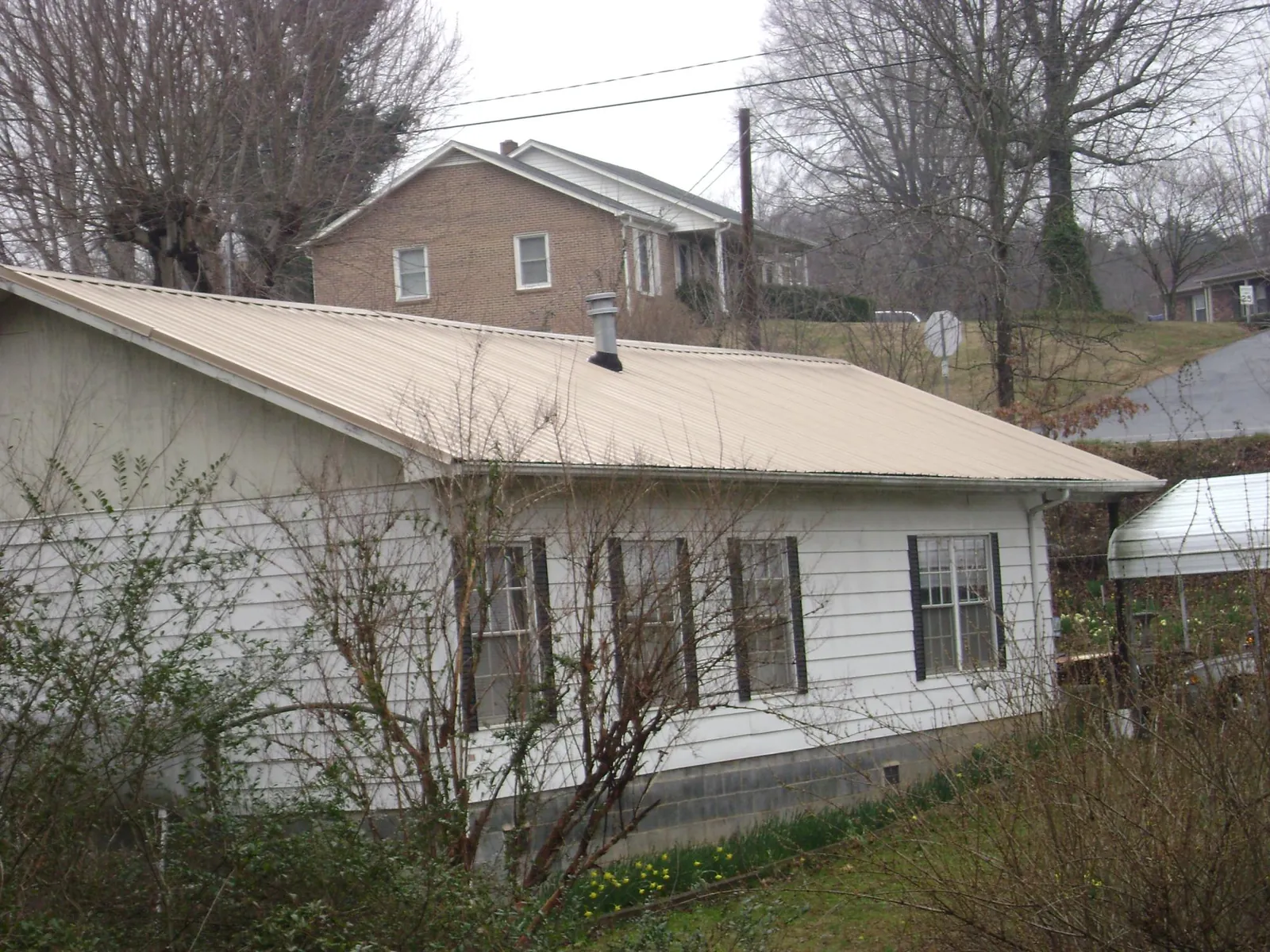 Tan metal roof on a white sided house set into a hillside — Commercial Roofing by Roofing Brothers in Waite Park