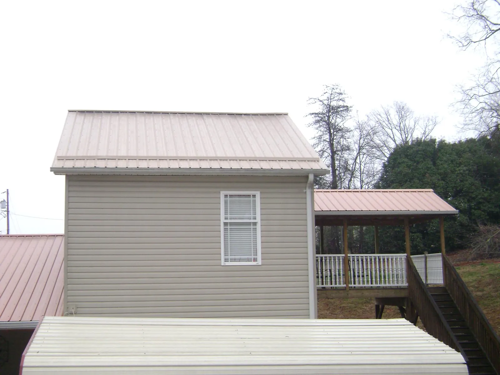 Tan metal roofs on a two story addition and attached porch, from a Roof Replacement job in Waite Park